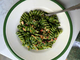 Green pasta dish on a white plate with a green rim, served on a marble surface.