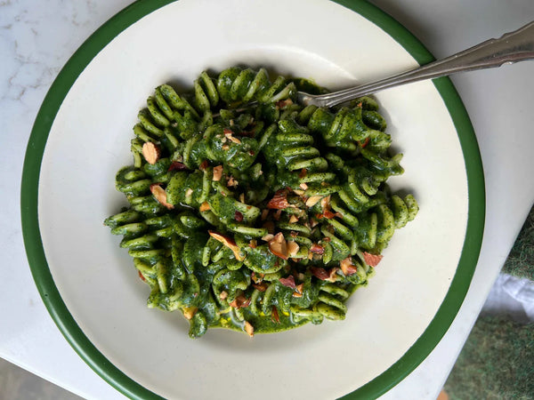 Green pasta dish on a white plate with a green rim, served on a marble surface.