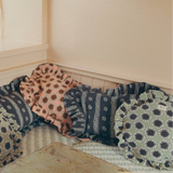 A cozy corner of a room with a built-in bench cushioned in patterned pillows, with a rustic table in the foreground holding a loaf of bread and a bowl of eggs.