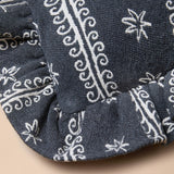 Close-up of a dark gray fabric product with white woven floral and scroll patterns, showing a ruffled edge against a light beige background.