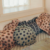 A cozy corner of a room with a built-in bench cushioned in patterned pillows, with a rustic table in the foreground holding a loaf of bread and a bowl of eggs.