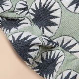 A close-up of a textured fabric with a repeating sunburst or starburst pattern in dark charcoal gray and white over a muted sage green background.