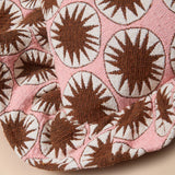 A close-up of a pink woven textile with a repeating brown and off-white sunburst pattern, draped to show texture and fold detail.