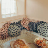 A cozy corner of a room with a built-in bench cushioned in patterned pillows, with a rustic table in the foreground holding a loaf of bread and a bowl of eggs.