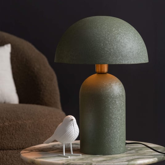 Green table lamp on a marble surface with a bird figurine in a dark room.