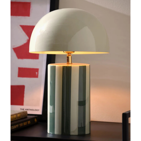 Table lamp with a green and white striped base and gold accents on a shelf.