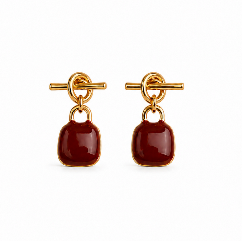 A pair of gold-tone drop earrings with a toggle clasp and a smooth, rounded dark red cabochon stone, shown on a plain white background.