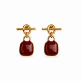 A pair of gold-tone drop earrings with a toggle clasp and a smooth, rounded dark red cabochon stone, shown on a plain white background.