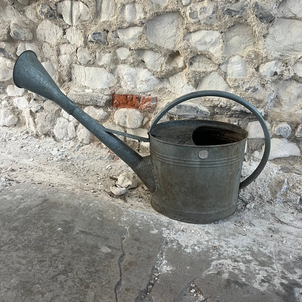Vintage metal watering can on a stone surface with a stone wall background