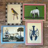 Four framed vintage-style animal and nature prints arranged on a rustic wooden wall. The prints show a bird, an elephant, a cheetah with mountains, and a blue lobster, each in a different colored frame.