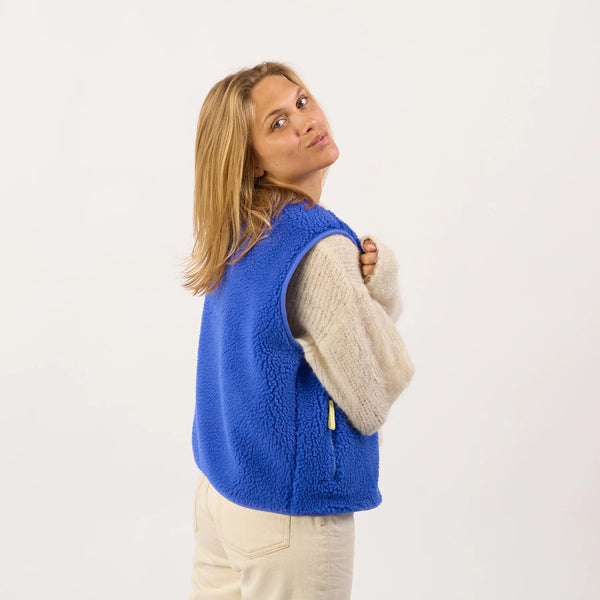 Woman wearing a blue fleece vest over a beige sweater on a white background
