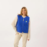 Woman wearing a blue vest with a small yellow logo on a white background