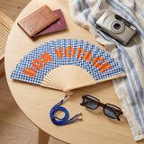 Bon Voyage fan on a table with sunglasses, camera, and travel items