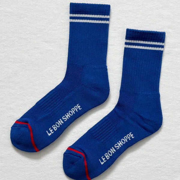 Pair of blue socks with white stripes and 'Le Bon Shoppe' branding on a light gray background