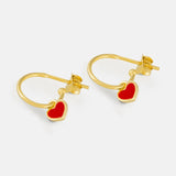 Gold hoop earrings with red heart charms on a light gray background