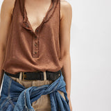 Woman wearing a brown sleeveless top with a deep neckline, beige pants, and a blue denim jacket over her shoulder on a white background.