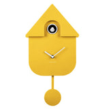 A bright yellow cuckoo clock shaped like a house, with a house-shaped body, house-top roof, white clock hands, a small circular window with a white bird silhouette, and a hanging round weight below. The brand name CARLSON is printed near the center.