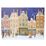 A square art print or panel depicting a snowy winter street scene with colorful historic buildings, snow-covered rooftops, pedestrians, and a deep blue night sky with falling snow.