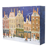 A rectangular advent calendar box featuring a winter city street scene with snow-covered buildings, pedestrians, and a dark blue night sky, photographed on a plain white background.