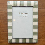 A rectangular picture frame with a striped border in sage green, cream, and white, displayed on a brown wooden surface. The center insert shows the brand name 'natalini'.