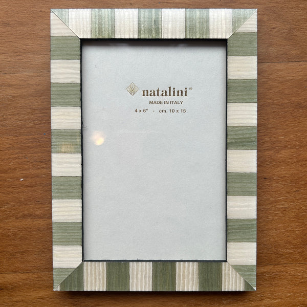 A rectangular picture frame with a striped border in sage green, cream, and white, displayed on a brown wooden surface. The center insert shows the brand name 'natalini'.