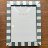 A rectangular picture frame with alternating blue and cream vertical stripes, shown on a wooden tabletop. The frame is empty, with a clear protective cover over the insert.