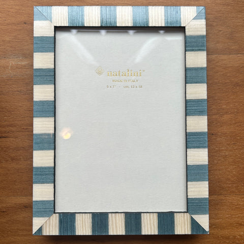 A rectangular picture frame with alternating blue and cream vertical stripes, shown on a wooden tabletop. The frame is empty, with a clear protective cover over the insert.
