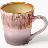 A ceramic coffee mug with a marbled glaze transitioning from a warm amber-brown rim to a dusty pink and mauve body, with a speckled purple base and a small chipped detail on the handle.