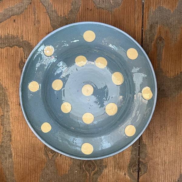 A round blue-gray ceramic bowl with a pattern of small gold polka dots, photographed from directly above on a rustic wooden surface.