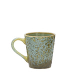 A handmade ceramic mug with a textured, speckled glaze transitioning from a light blue-green at the top to a warm brown at the base, featuring a rustic yellow-green rim and handle.