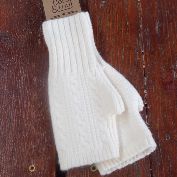 A pair of cream cable knit fingerless gloves laid flat on a wooden surface.