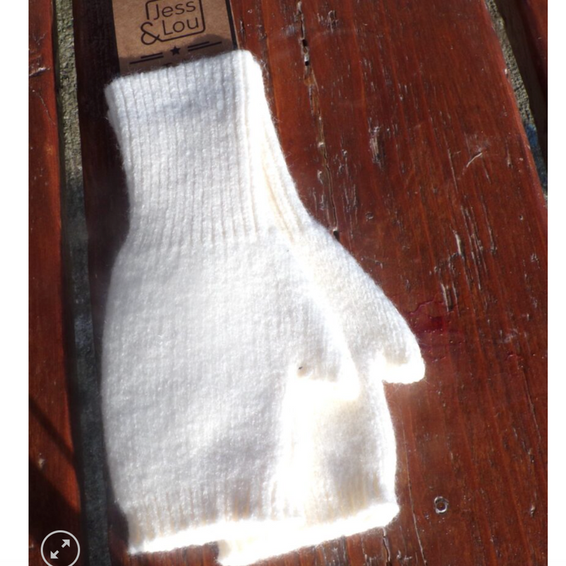 A cream-colored fingerless knit glove displayed on a wooden surface with the brand 'Jess & Lou' visible on the tag.